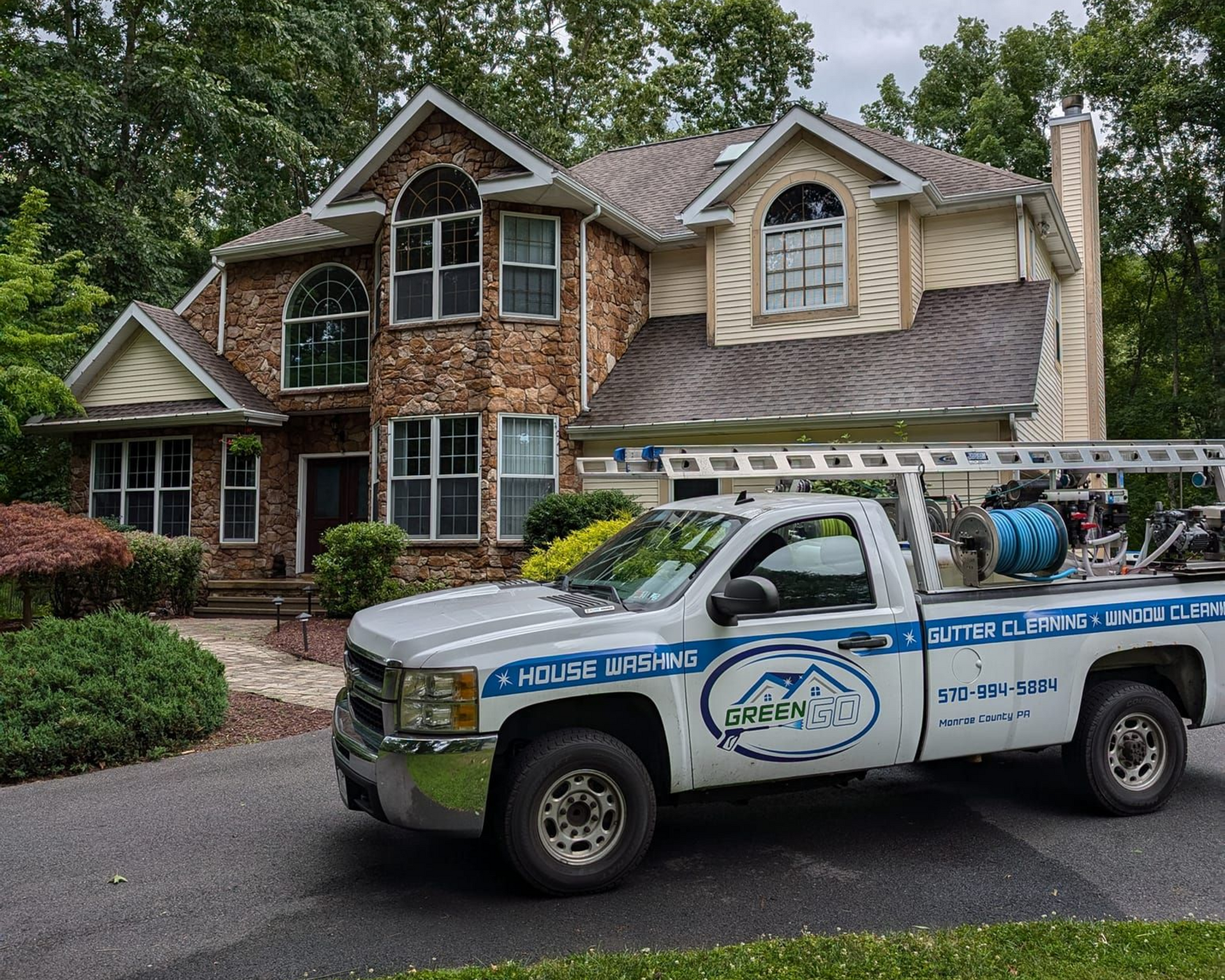 Truck parked in front of a house, likely for roof cleaning. House has stone and beige siding. Overcast day.