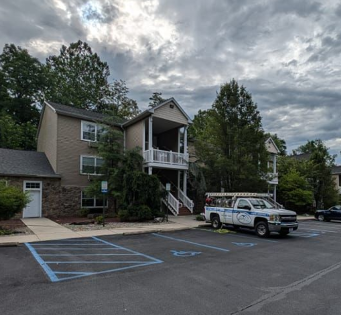 Two-story building with a porch, next to a parking lot with a work truck on an overcast day.