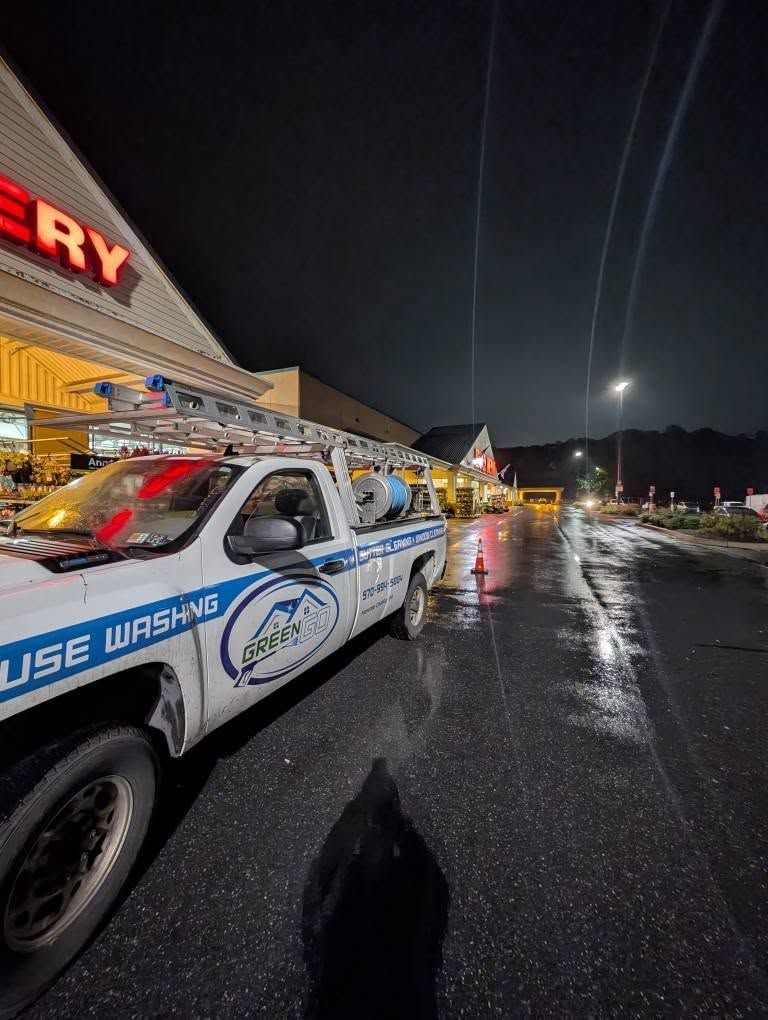 A white house washing truck parked in front of a grocery store at night. Reflective wet pavement.