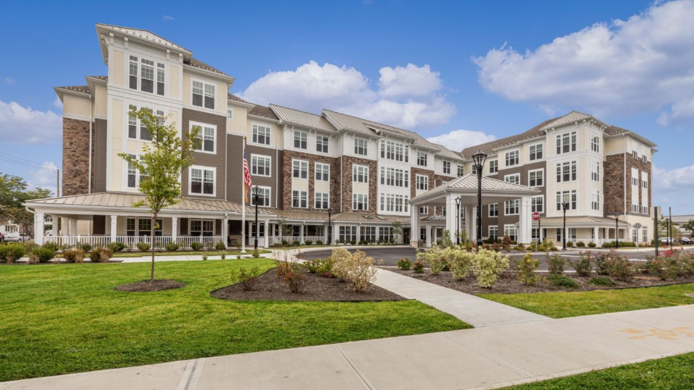 Multi-story apartment building with blue and gray siding, trees, and a walkway on a sunny day.