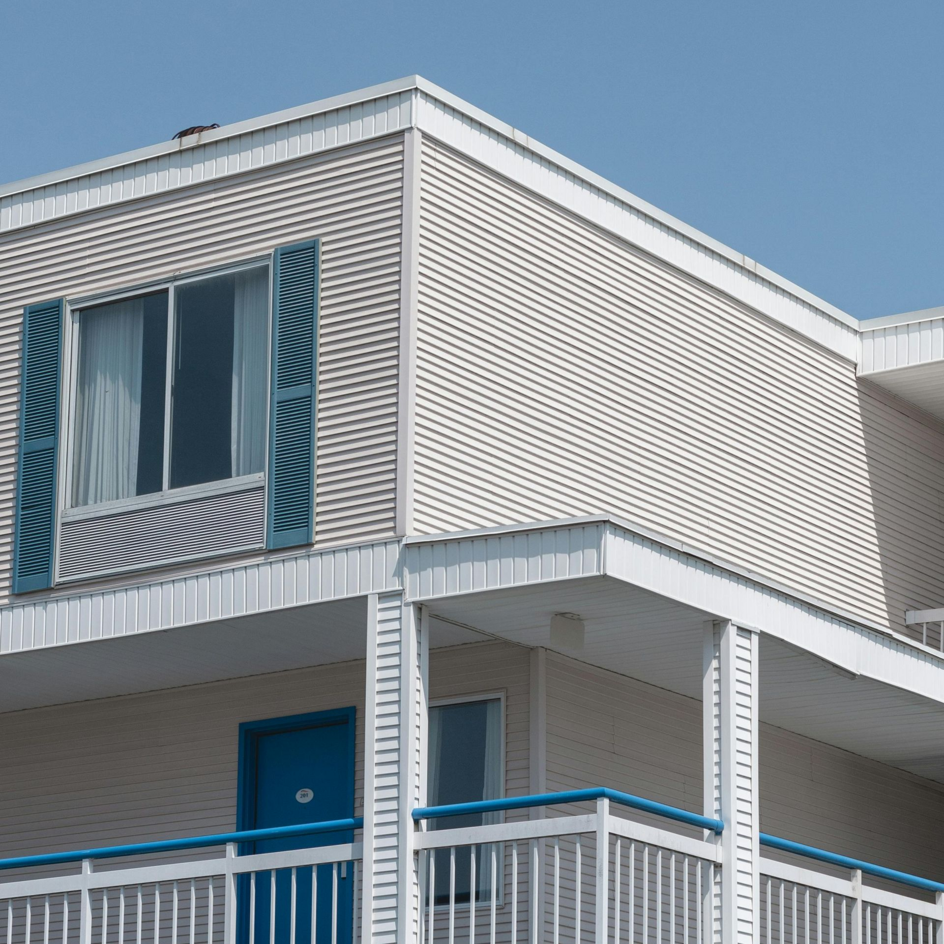 Exterior of a motel; two-story building with blue trim and doors, white siding, blue sky.