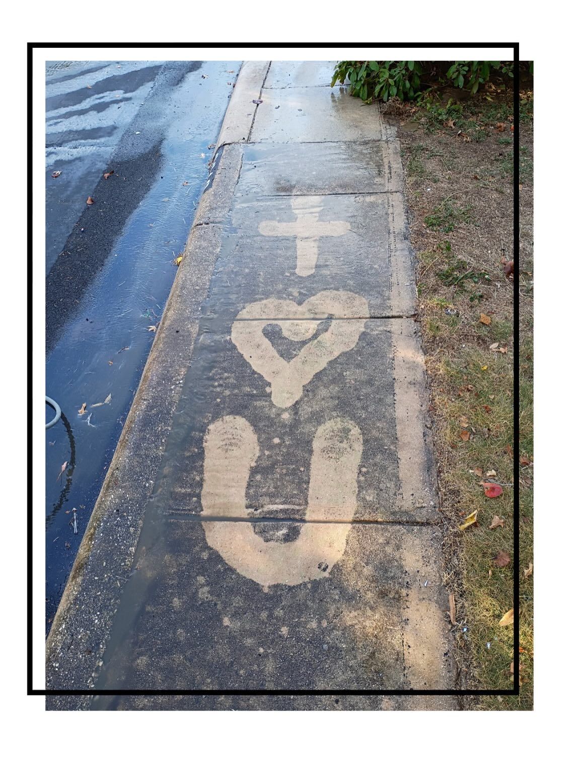 A message drawn in wet sand or chalk on a sidewalk featuring a cross, a heart, and the letter U.