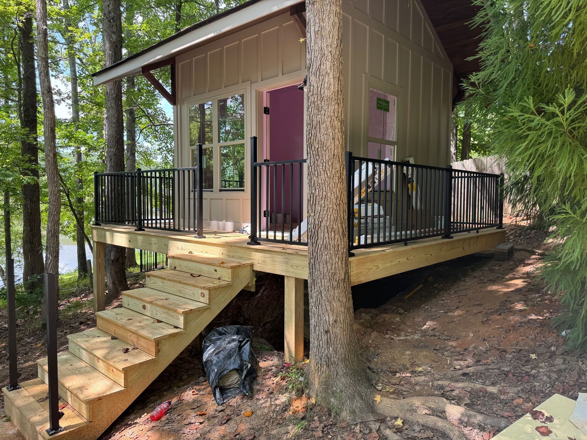 Small cabin with porch, stairs, and black railing in a wooded area