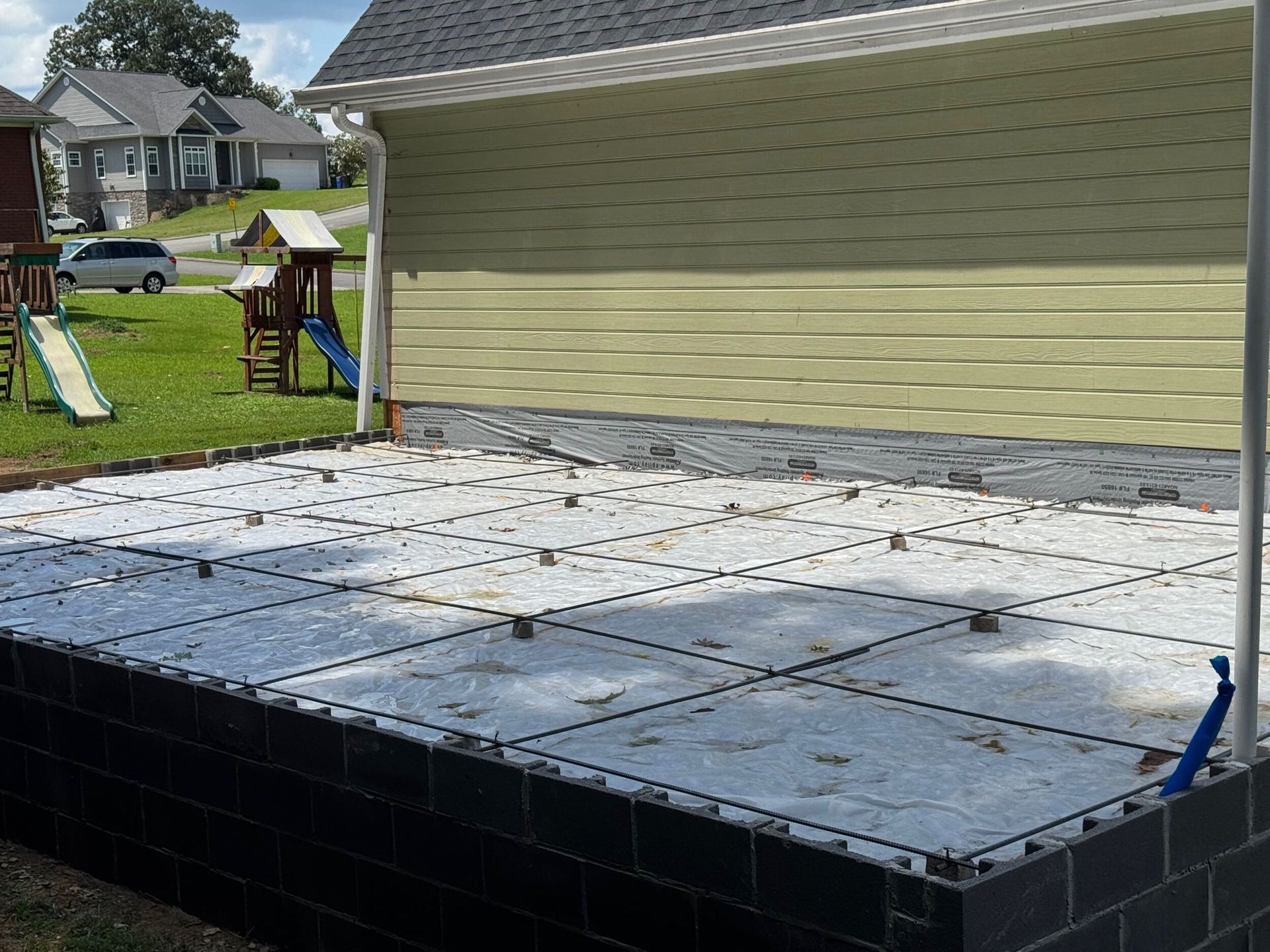 Backyard patio being built beside a house, with white deck panels and tools visible.