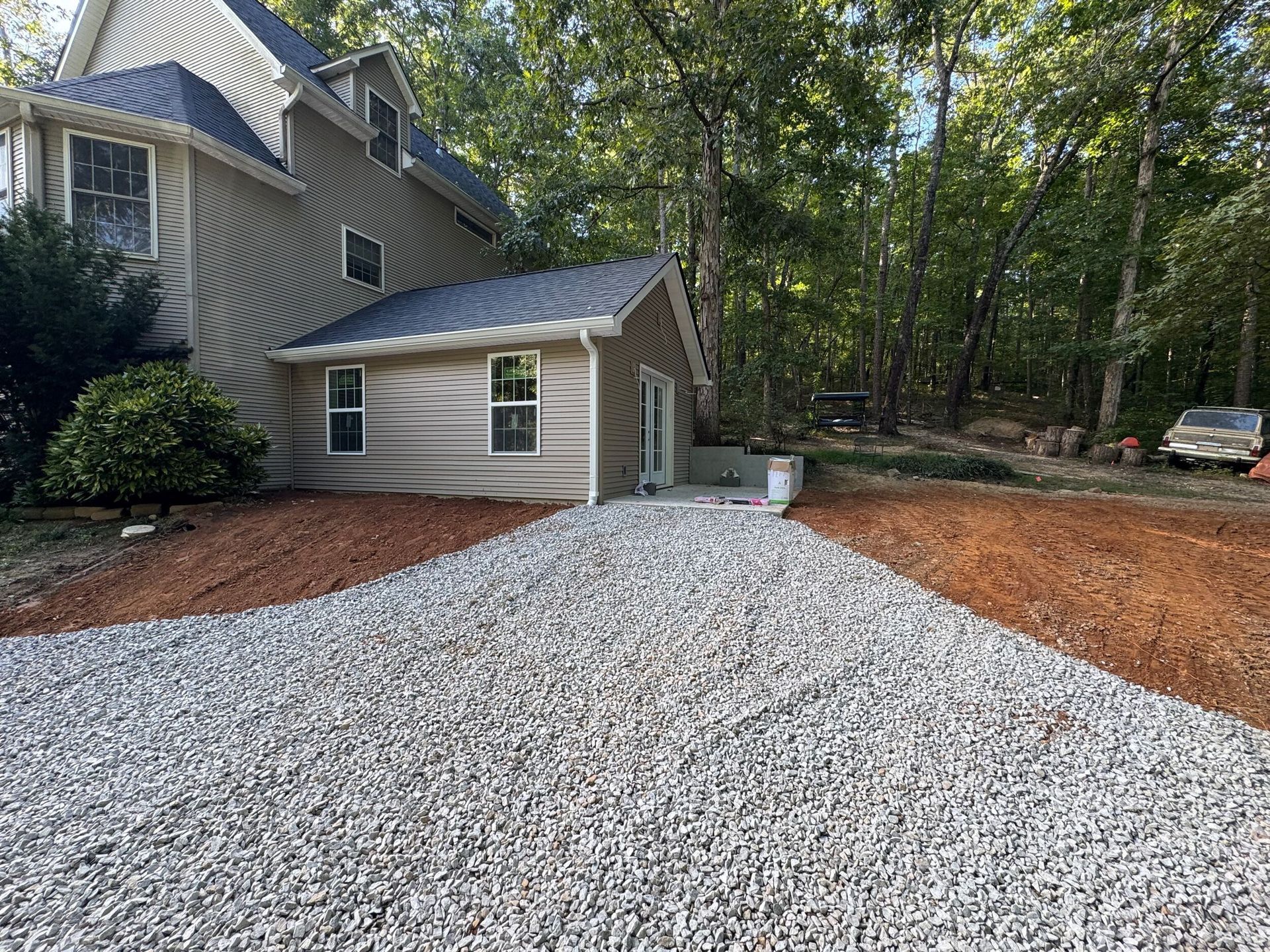 House with gray gravel driveway and red mulch beside wooded yard