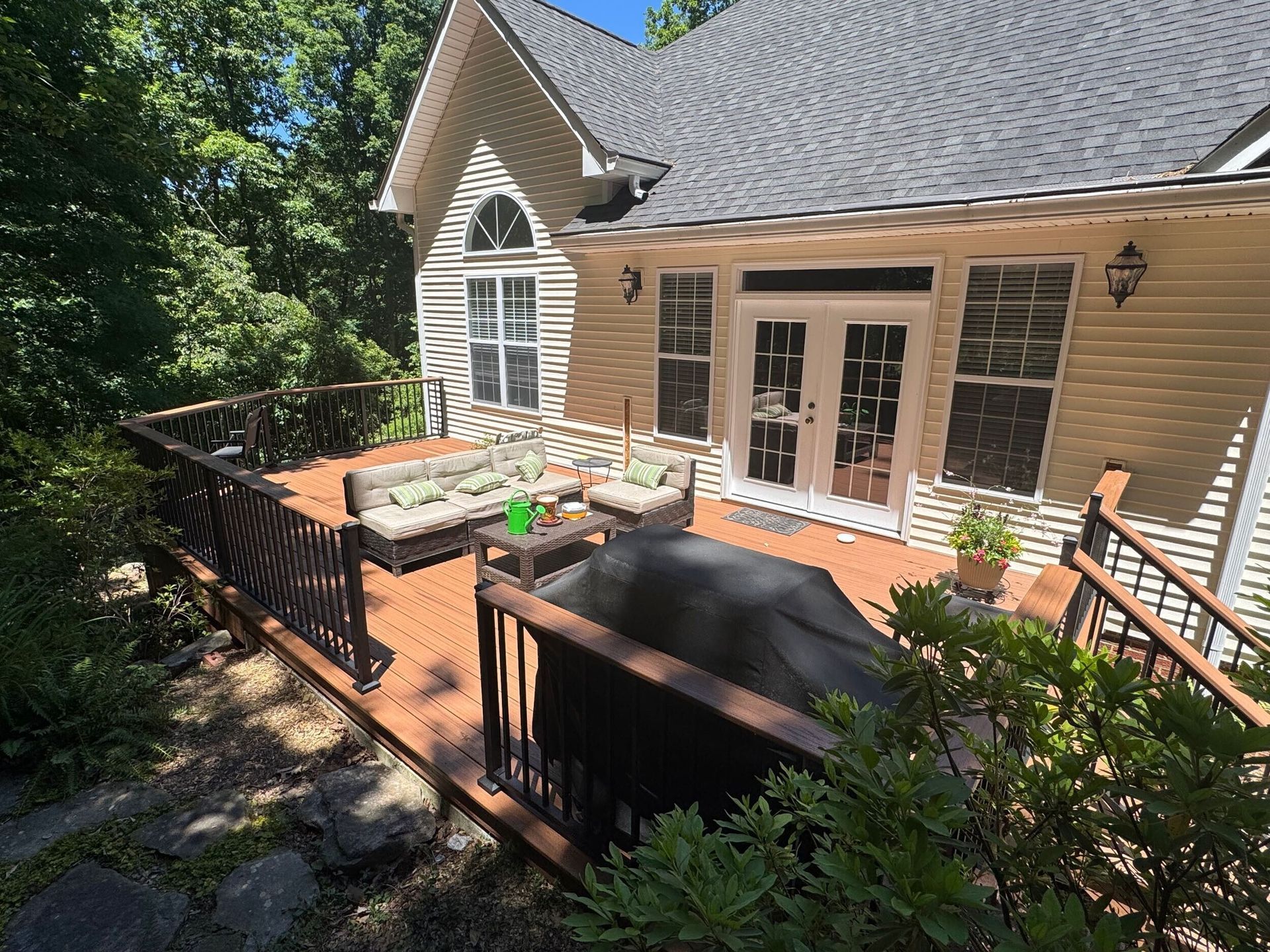 Back deck with black railing, patio table, tan siding, and French doors beside wooded yard