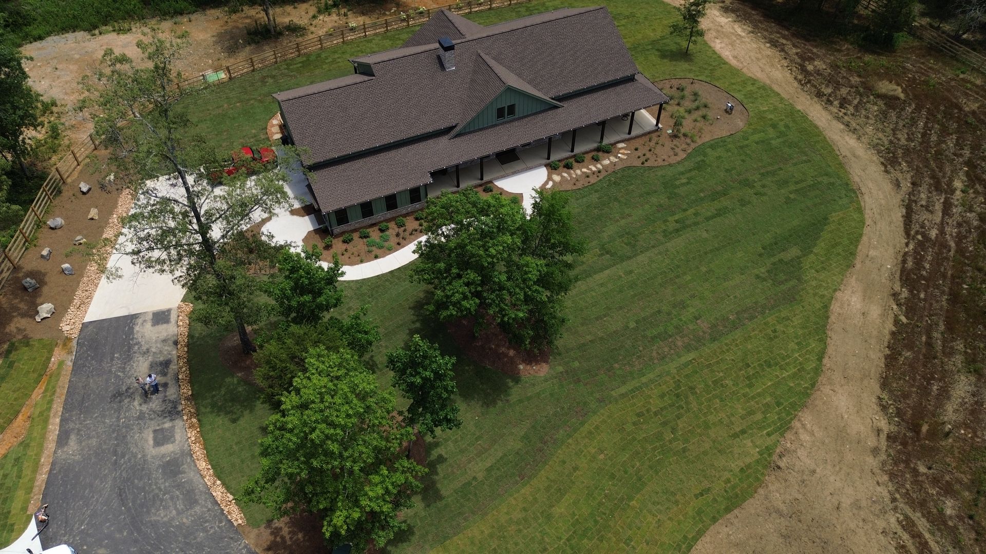 Aerial view of a house with a dark roof beside a curving driveway and green lawn.