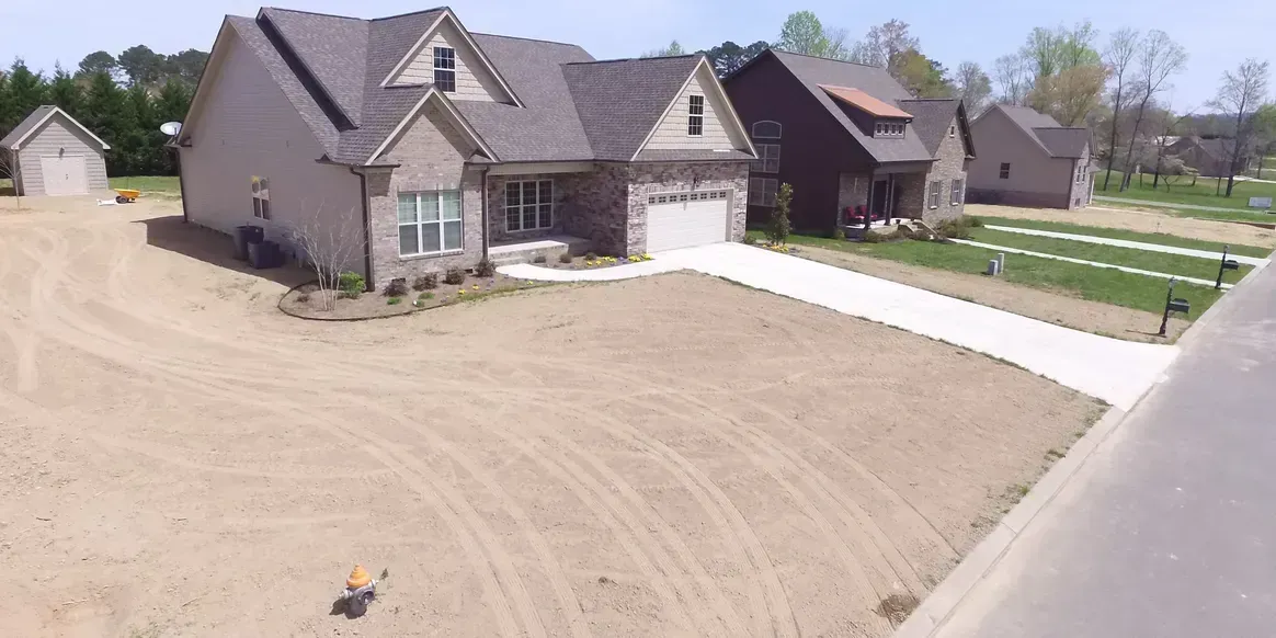 New house with unfinished dirt yard and concrete driveway in a suburban neighborhood