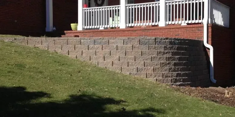 Brick house porch with white railings above a sloped grassy yard and steps