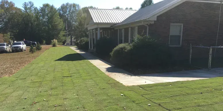 Brick house with white porch and driveway beside a freshly mowed green lawn