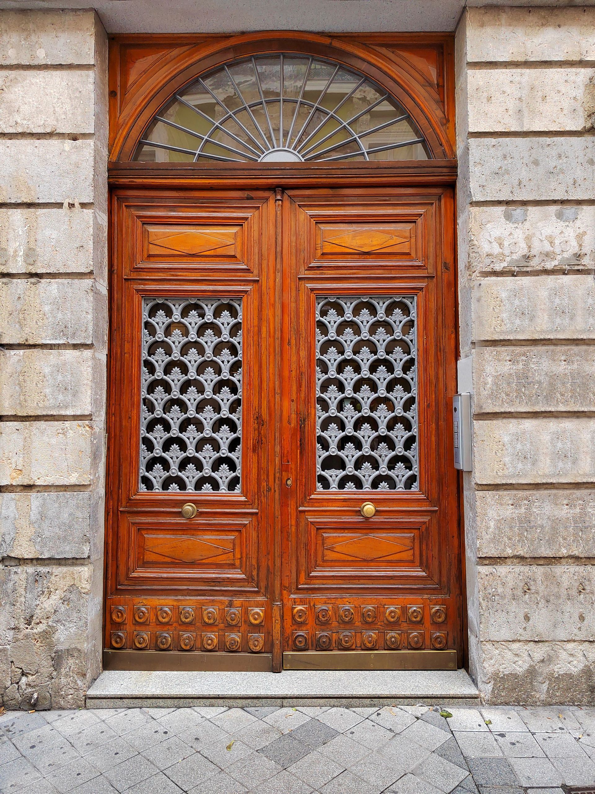 Wooden double door with ornate glass panels and arched fanlight in a stone facade