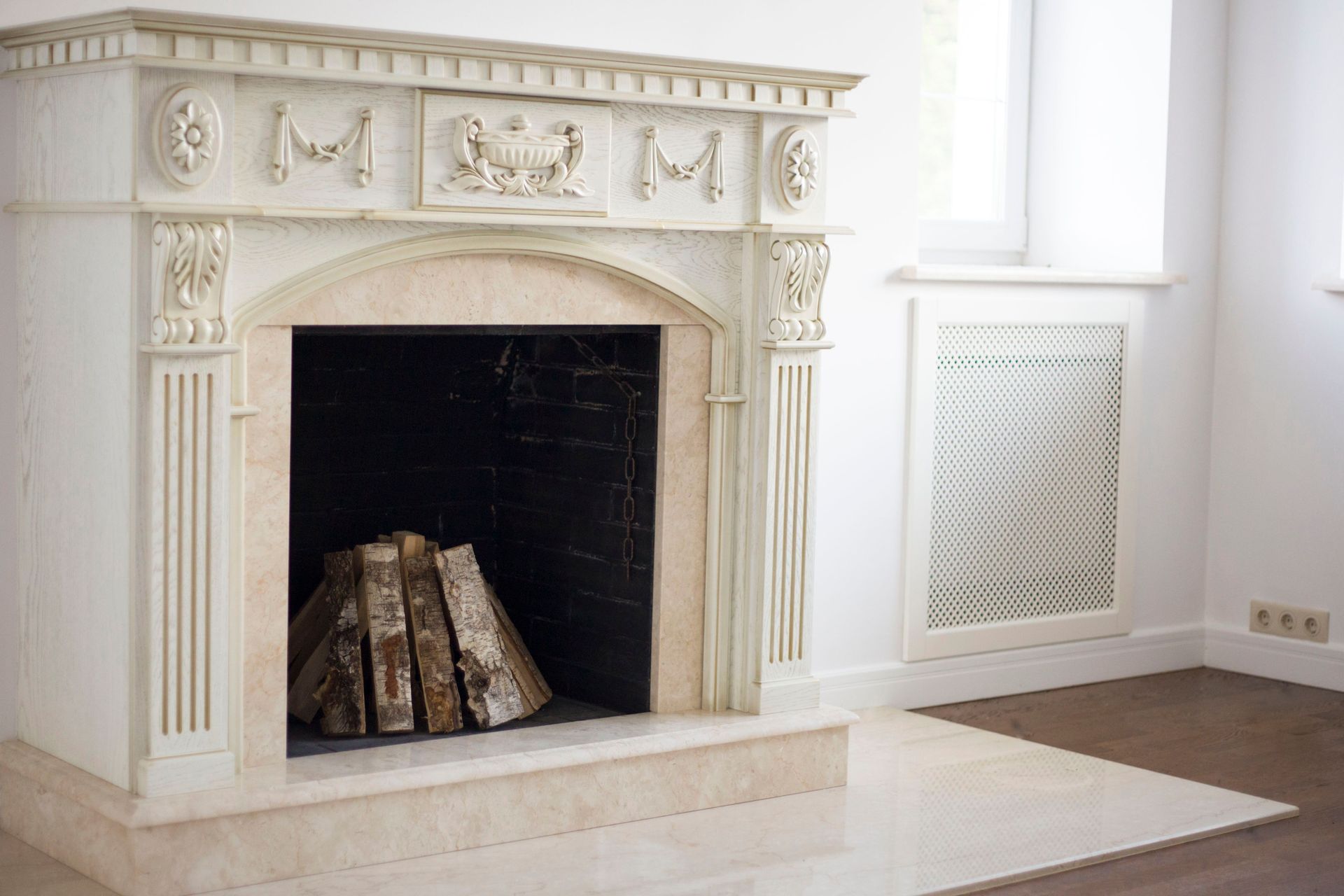White ornate fireplace with logs inside in a bright empty room