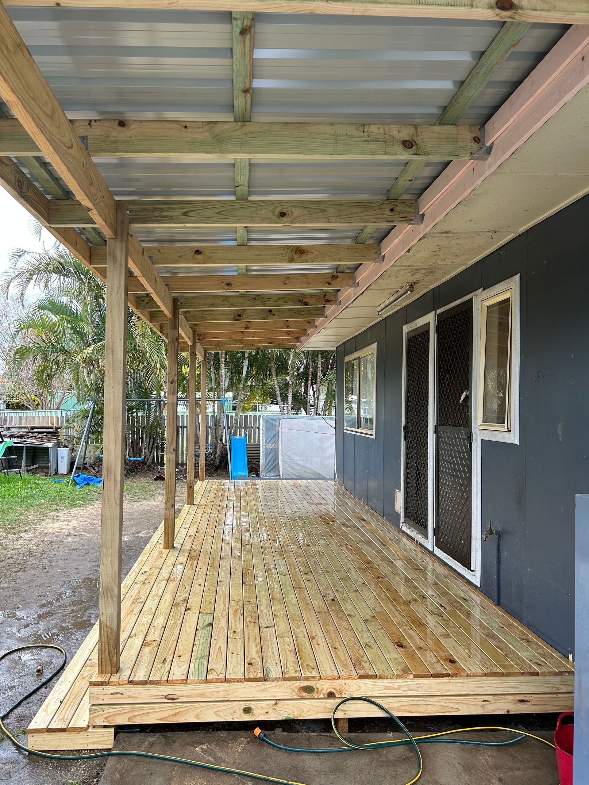 A Wooden Deck With a Metal Railing and a House in the Background — BK Build Group in Coffs Harbour, NSW