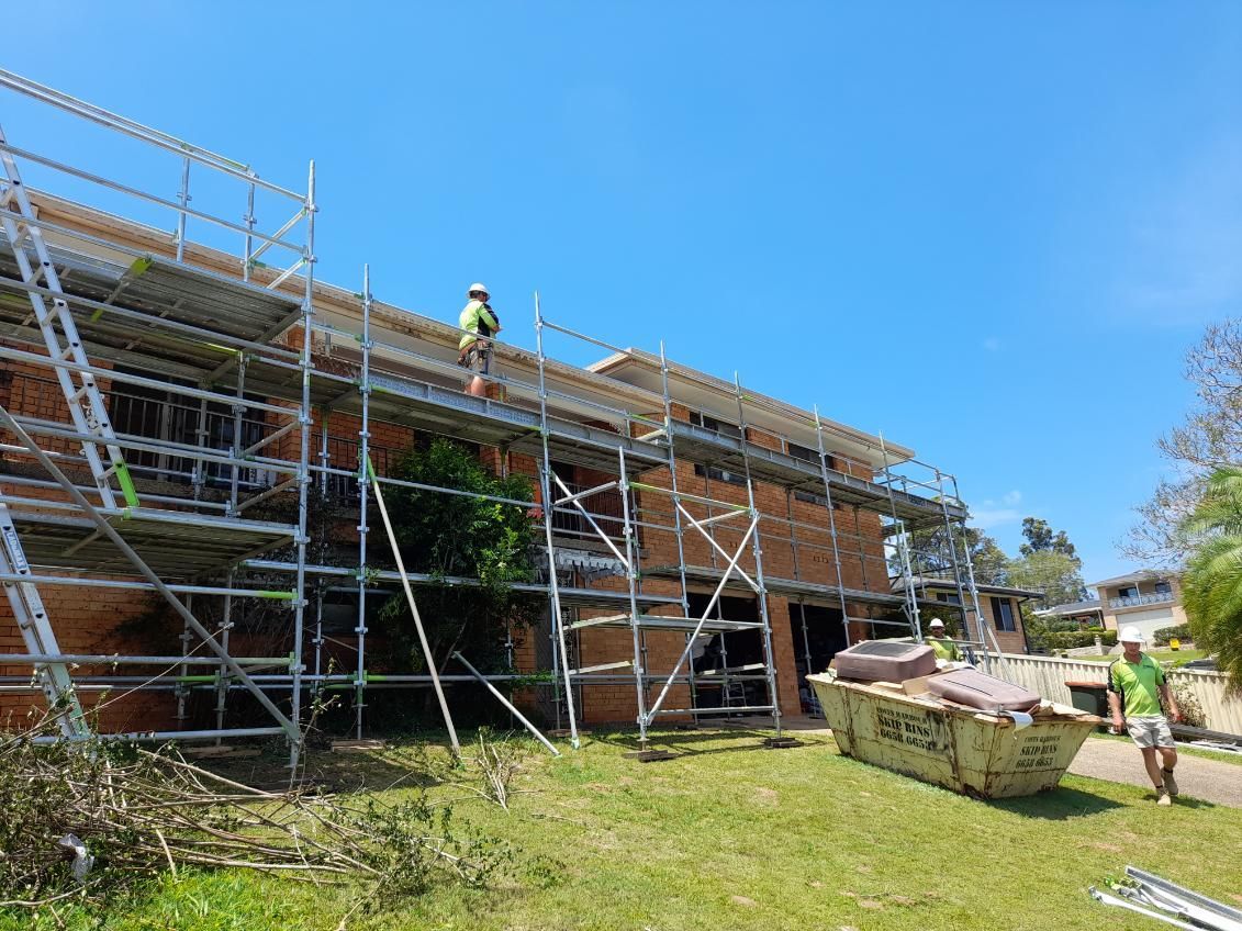 A Man is Standing on a Scaffolding on the Roof of a Building — BK Build Group in Nambucca Heads, NSW