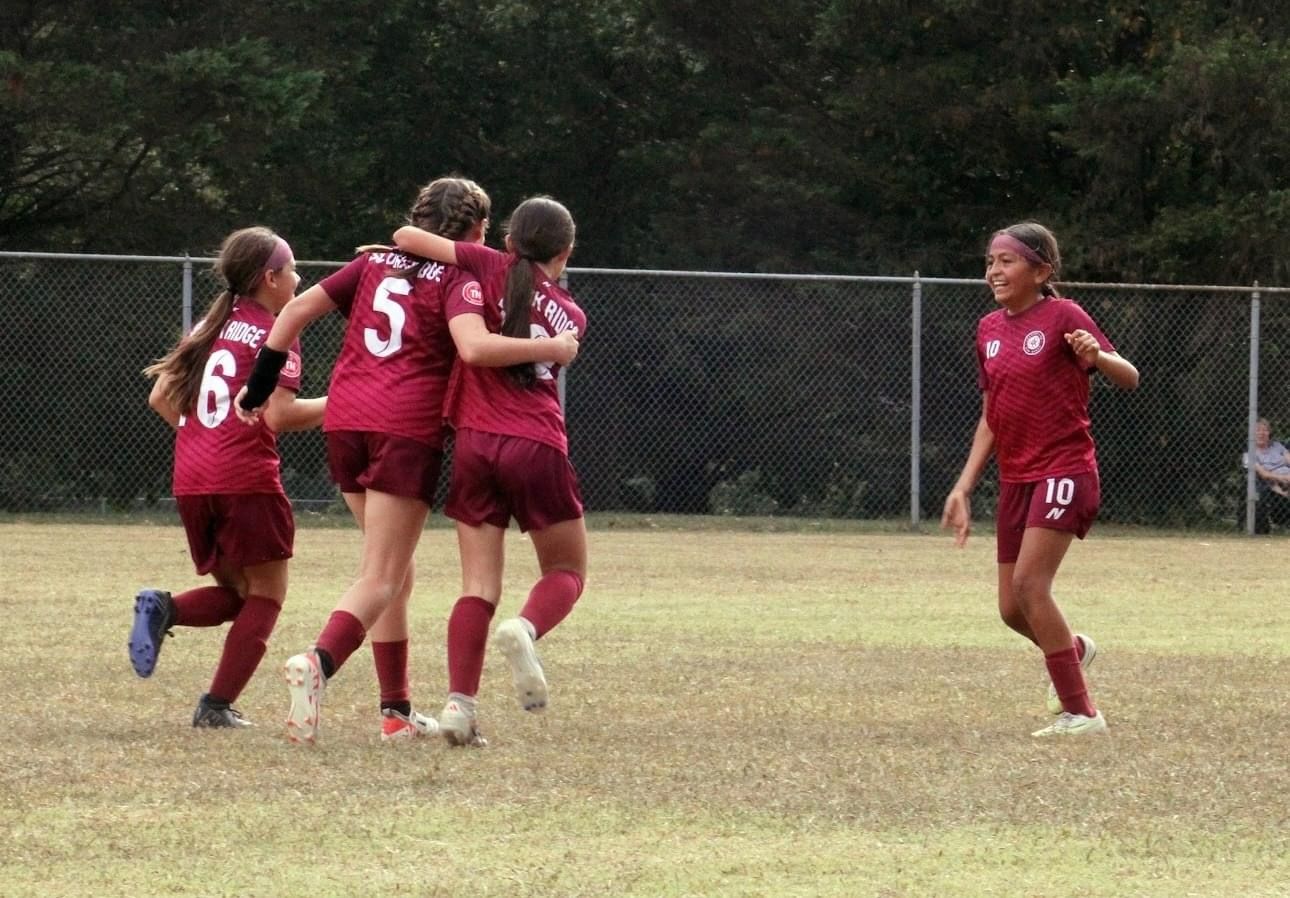 A group of SCOR girls are hugging each other on a soccer field.