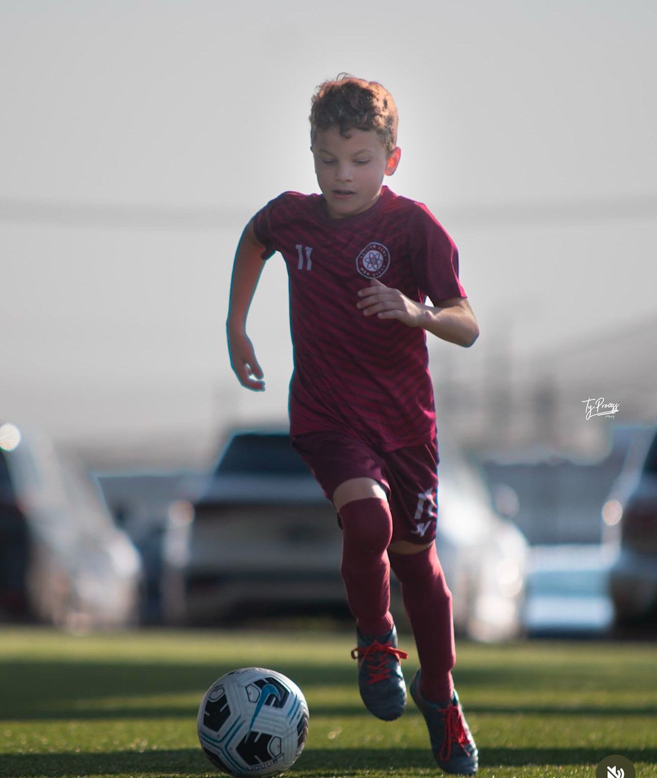 A young boy is running after a soccer ball on a field.