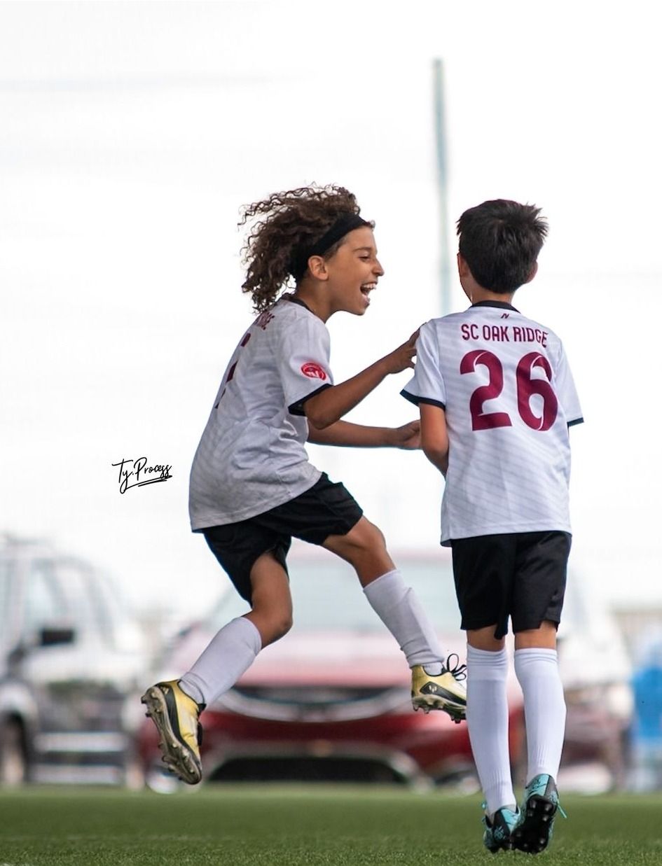 Two young boys are playing soccer and one of them has the number 26 on his shirt.
