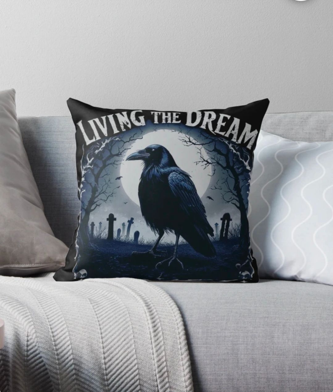 Black throw pillow with crow and “LIVING THE DREAM” on a gray couch with white pillows