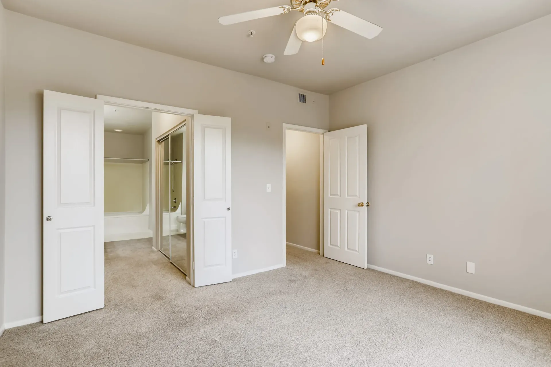 Bedroom with beige walls, white doors, ceiling fan, and beige carpet; closet and bathroom door visible at Alicante Apartments in Aliso Viejo, CA.