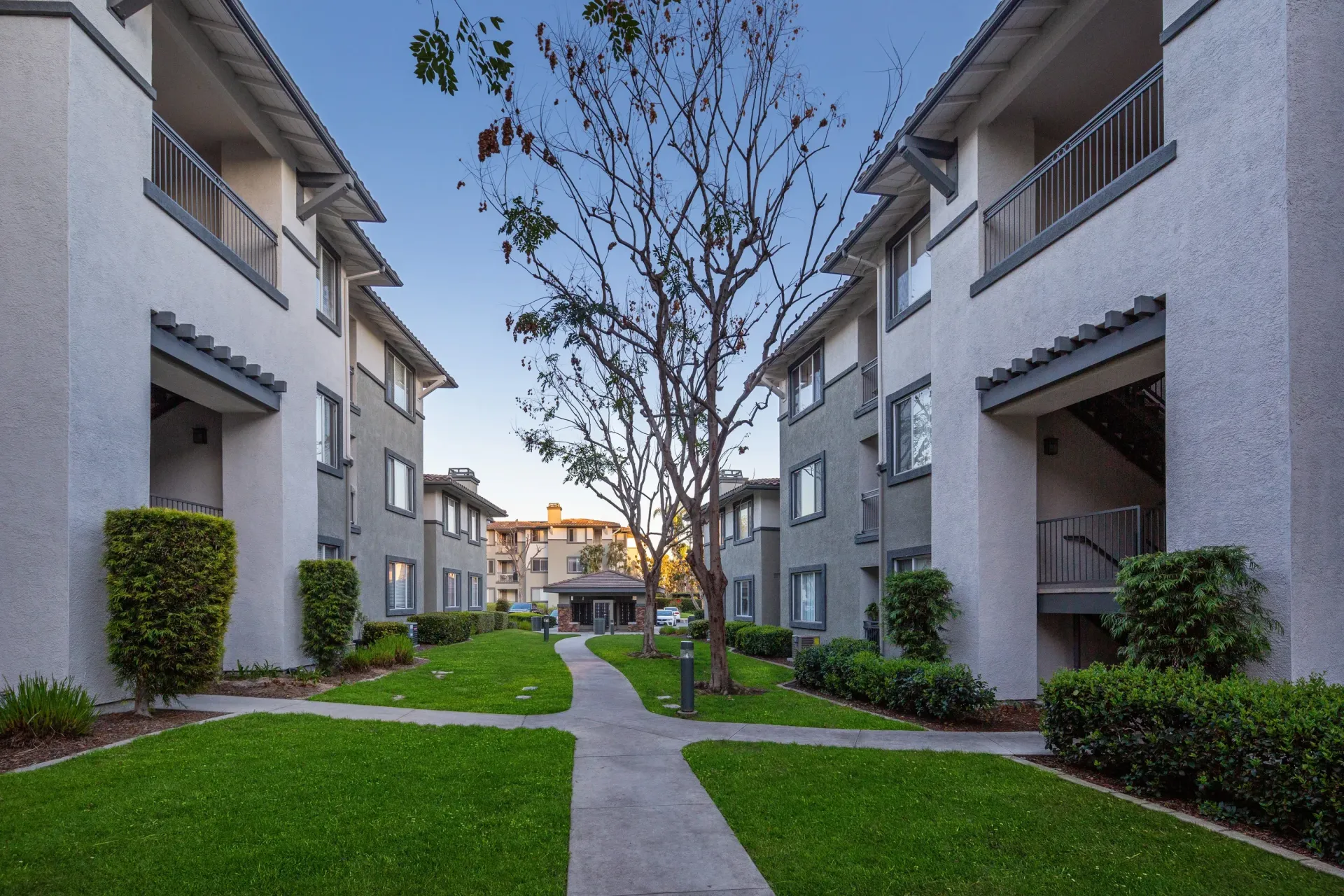 Exterior view of a multi-building apartment community with a central grassy courtyard and walkways at Alicante Apartments in Aliso Viejo, CA.