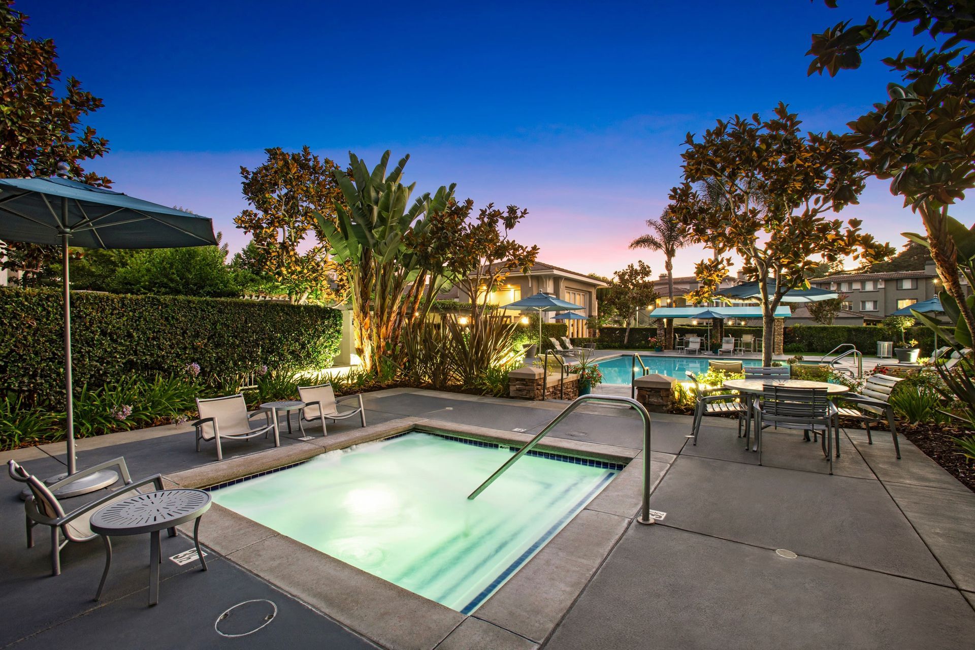 Outdoor community pool area with lounge chairs and umbrellas at dusk at Alicante Apartments in Aliso Viejo, CA.