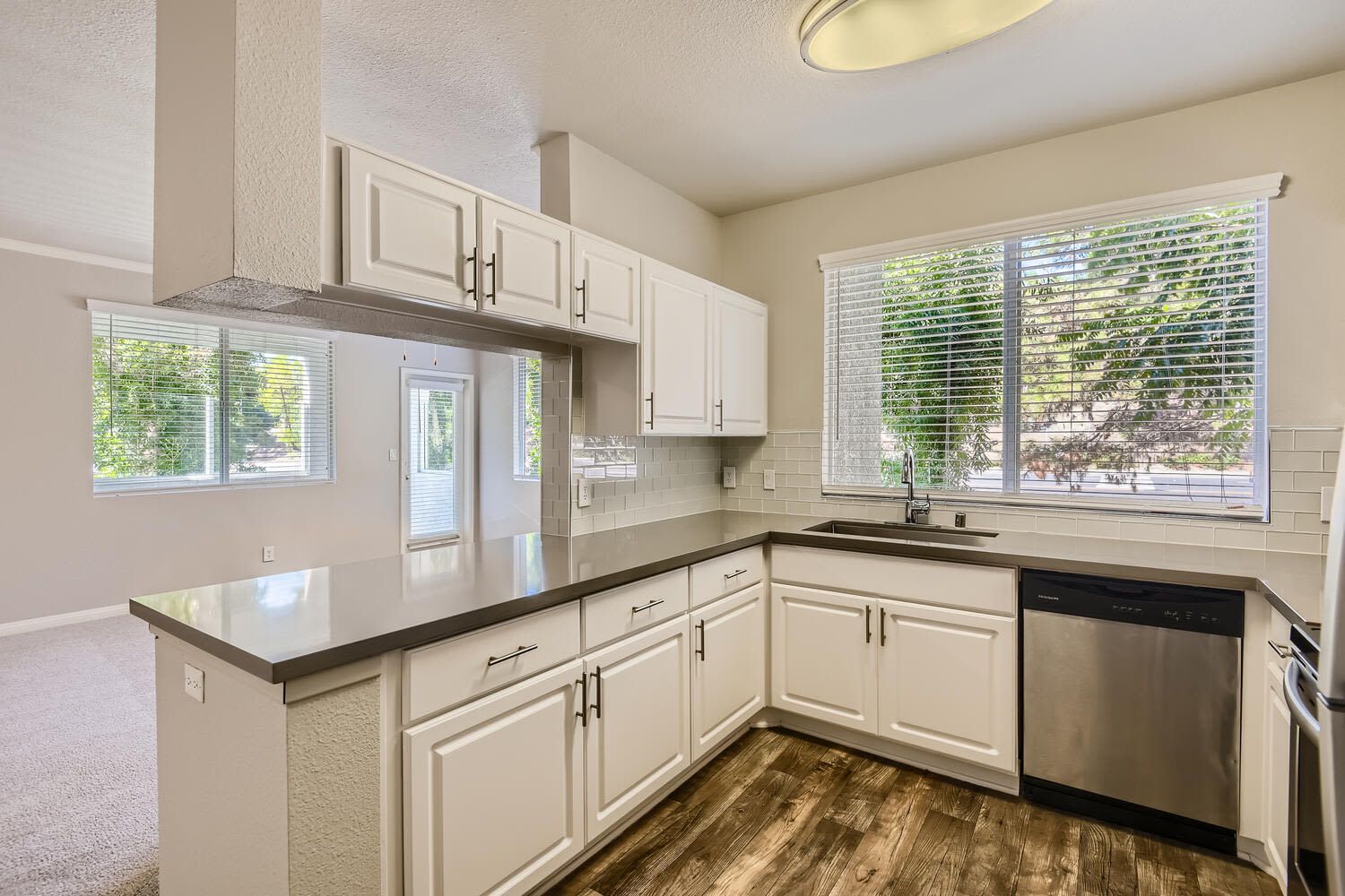 Bright kitchen with white cabinets, gray countertops, stainless steel dishwasher, and a large window over the sink at Alicante Apartments in Aliso Viejo, CA.