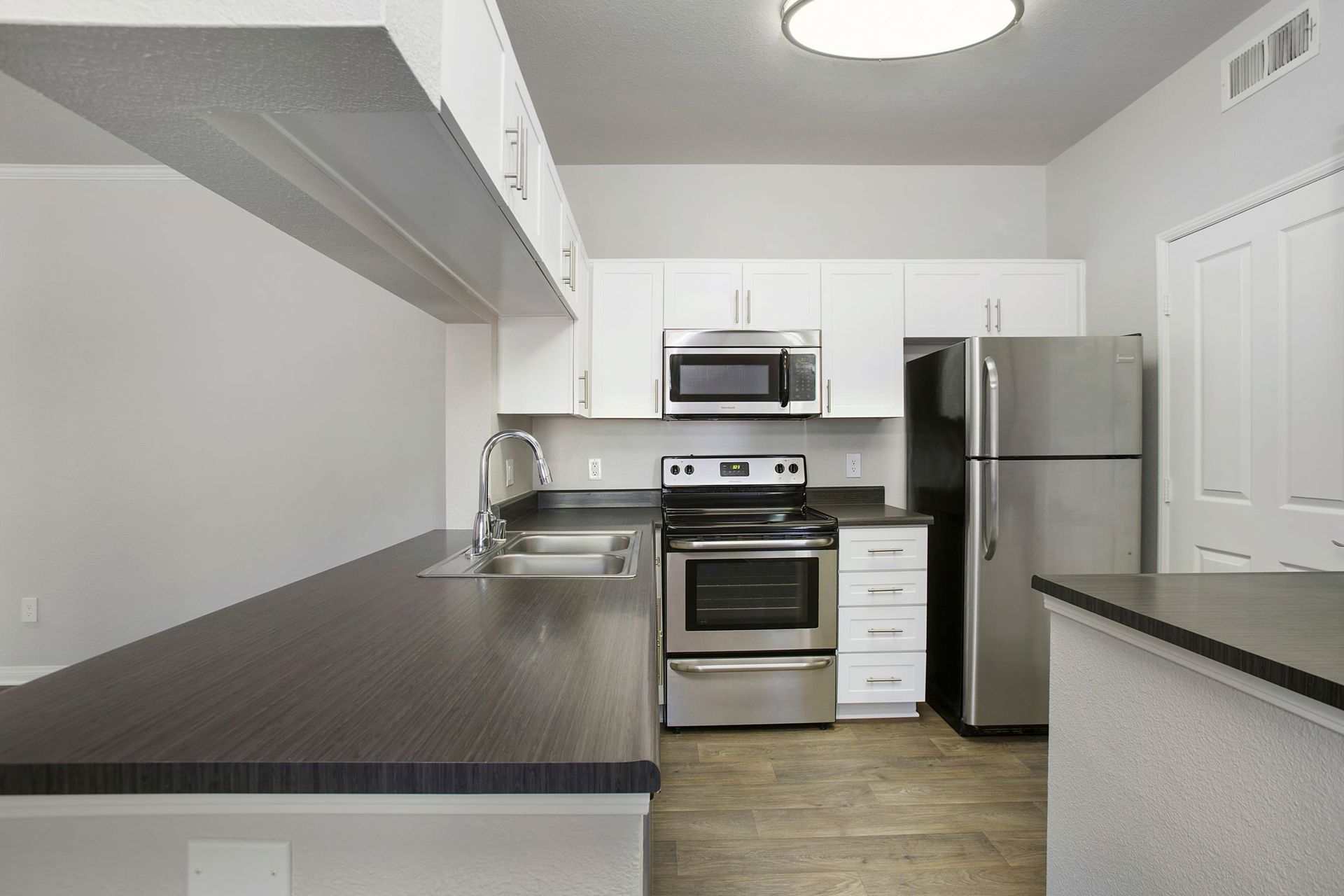 Modern kitchen in an apartment with white cabinets, stainless steel appliances, and dark countertops at Alicante Apartments in Aliso Viejo, CA.