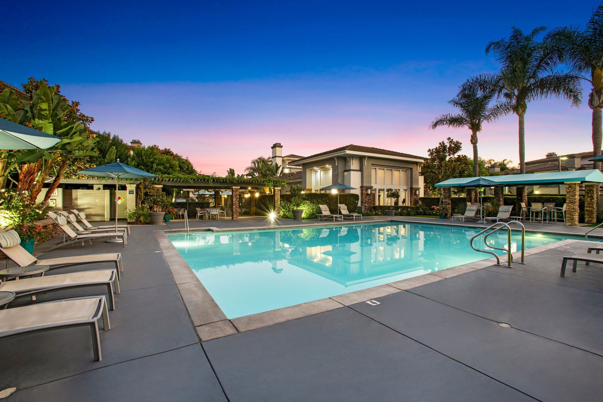 Outdoor community pool area with lounge chairs, umbrellas, and palm trees at Alicante Apartments in Aliso Viejo, CA.