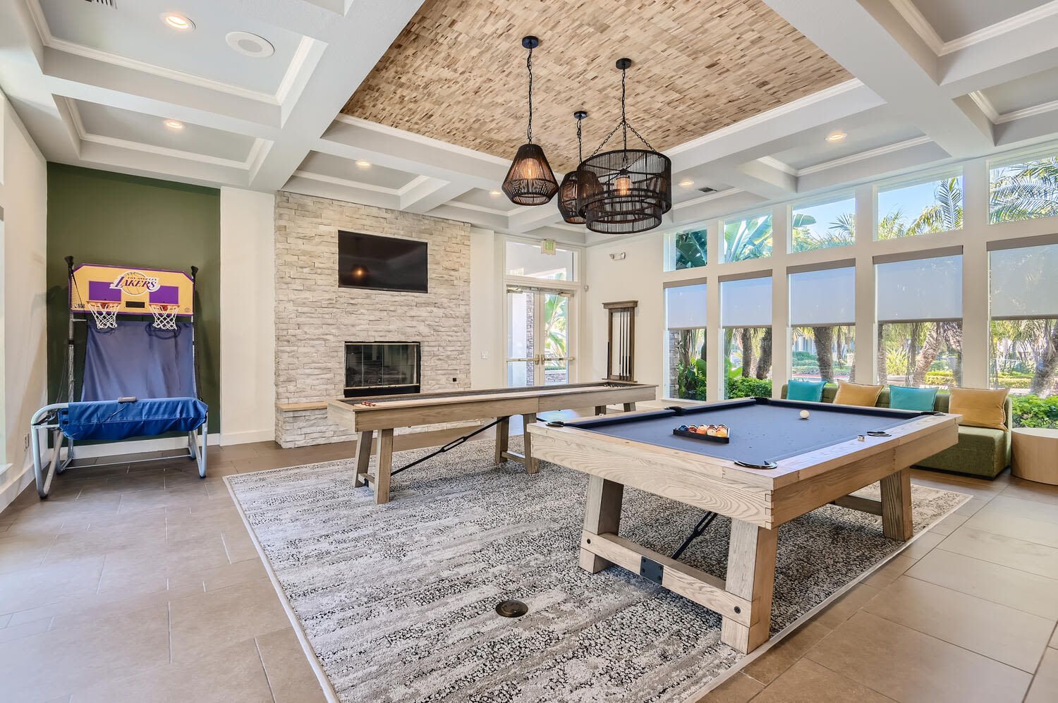 Indoor community game room with a pool table, long shuffleboard table, and seating by large windows at Alicante Apartments in Aliso Viejo, CA.