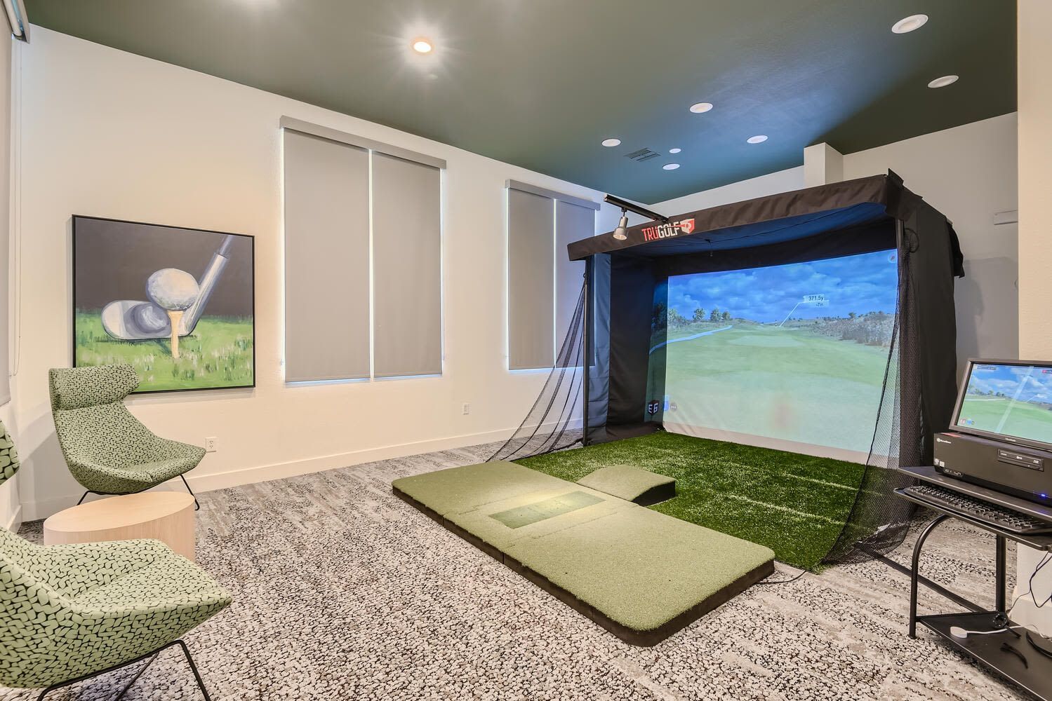 Indoor golf simulator in a recreation room with a large screen, turf mat, and seating at Alicante Apartments in Aliso Viejo, CA.