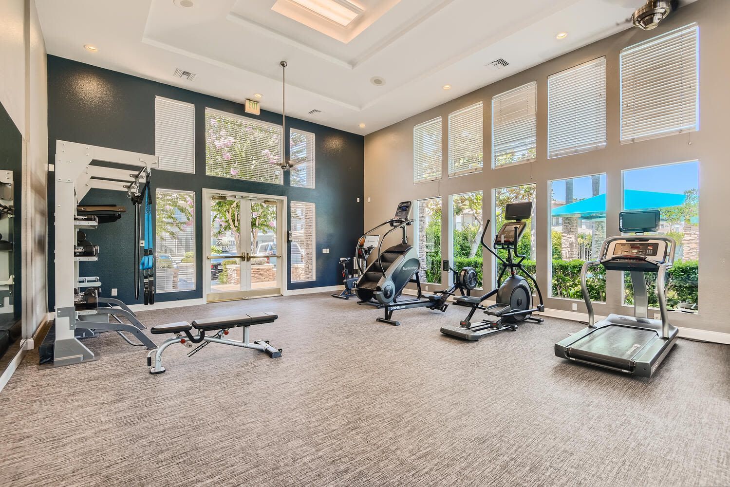Bright apartment community gym with cardio machines and a weight station by large windows at Alicante Apartments in Aliso Viejo, CA.