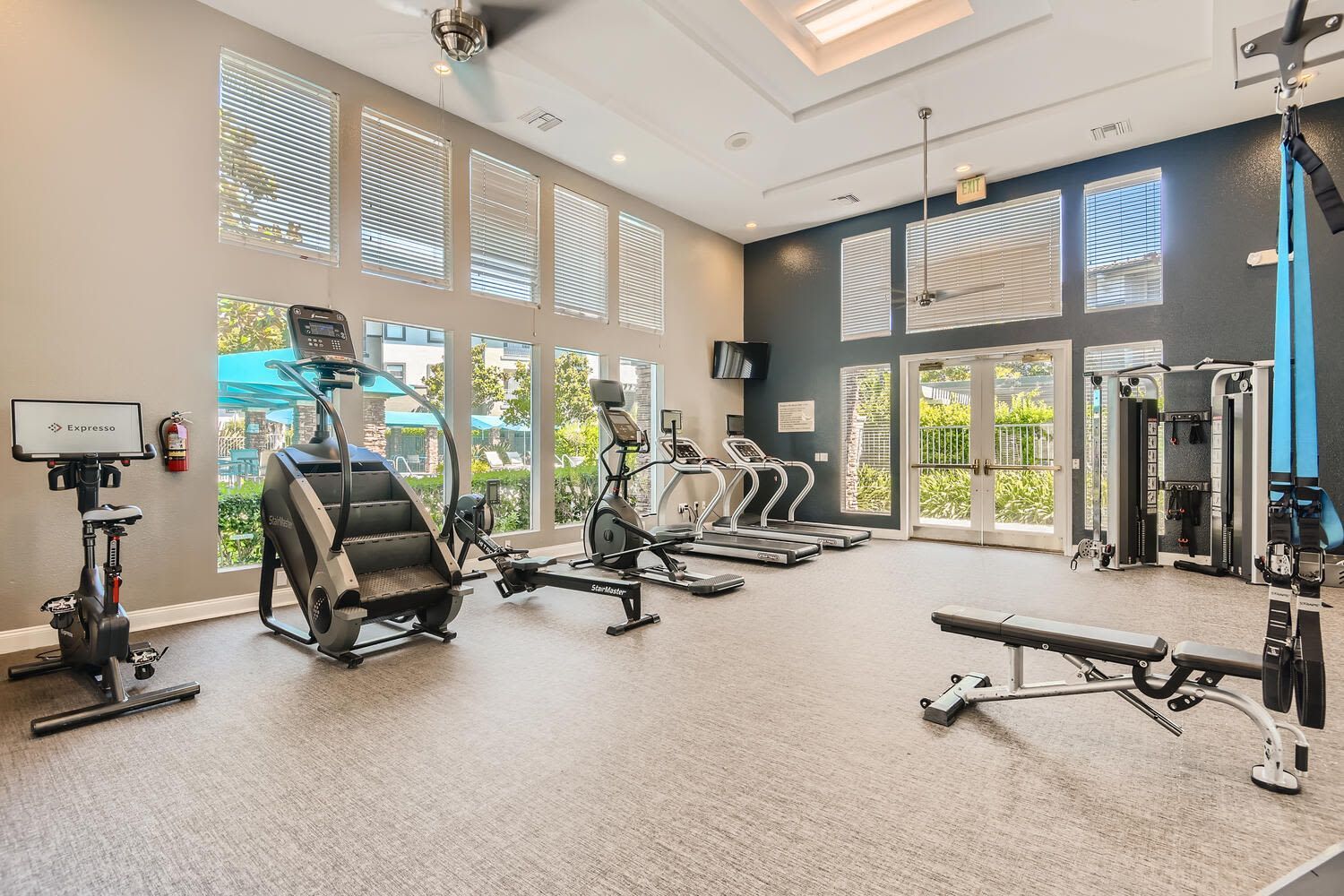Bright apartment fitness center with treadmills, bikes, and weight machines beside large windows at Alicante Apartments in Aliso Viejo, CA.
