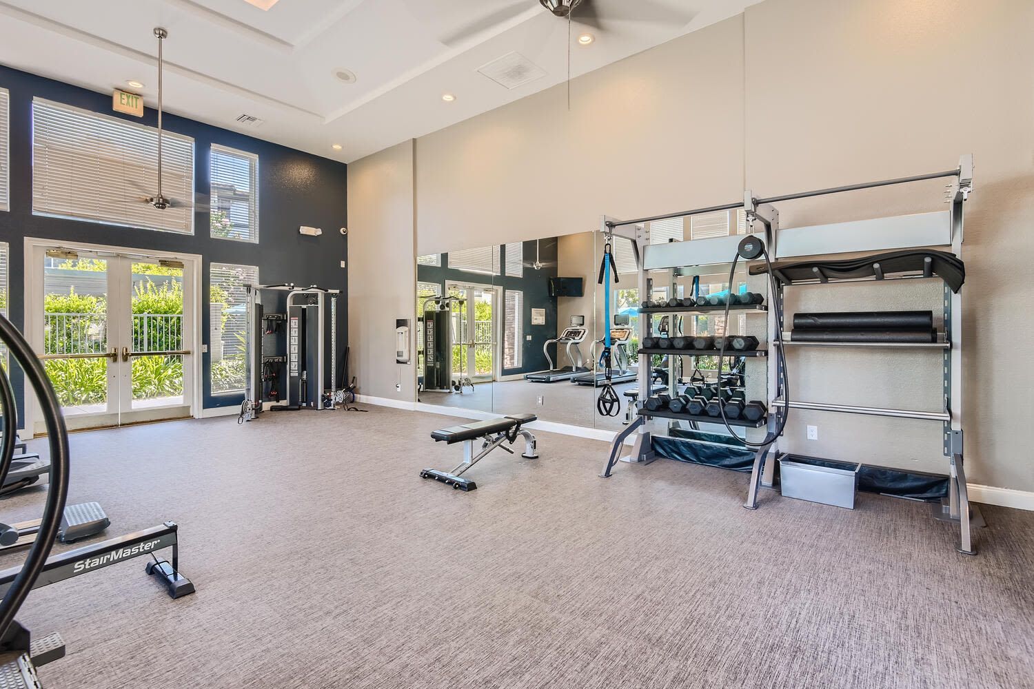 Well-lit community gym with free weights, a weight rack, treadmills, and a large mirror at Alicante Apartments in Aliso Viejo, CA.