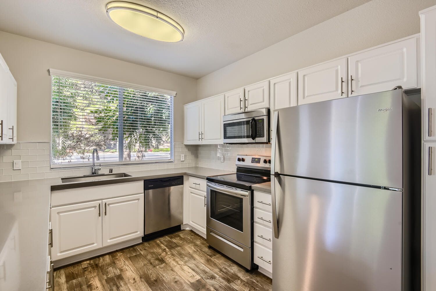 Modern apartment kitchen with white cabinets, stainless steel appliances, and a large window at Alicante Apartments in Aliso Viejo, CA.