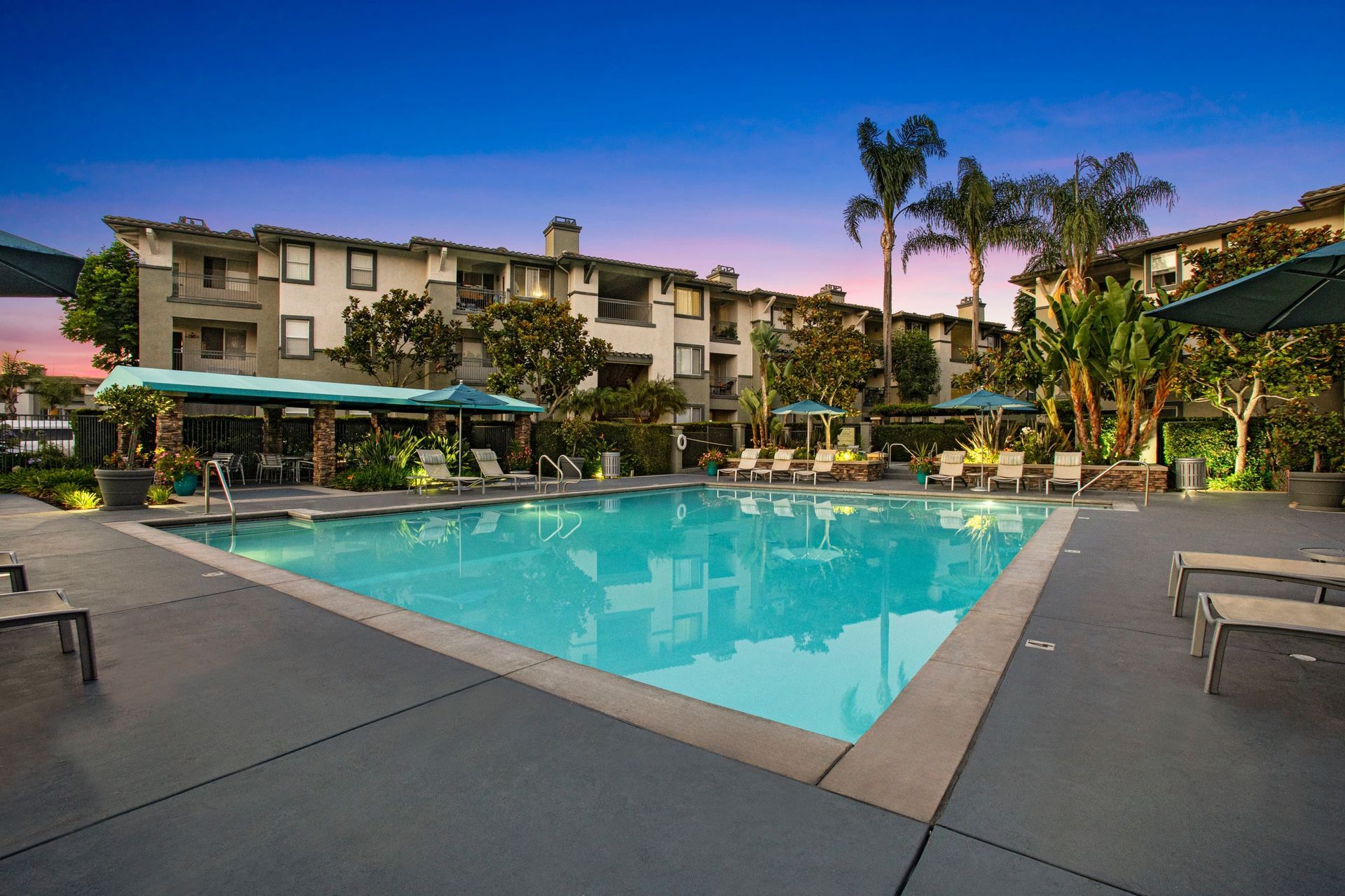 Outdoor apartment community pool with lounge chairs, umbrellas, and surrounding buildings at Alicante Apartments in Aliso Viejo, CA.