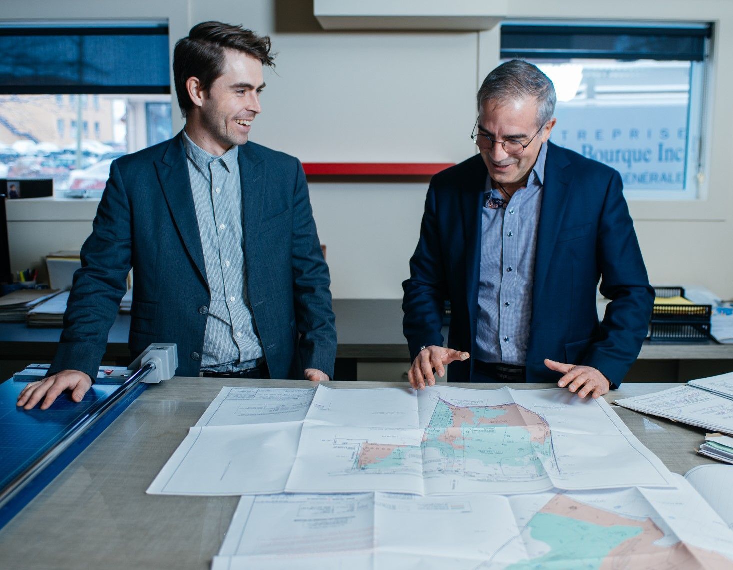 Deux hommes en costume examinent des plans sur un bureau dans un bureau.