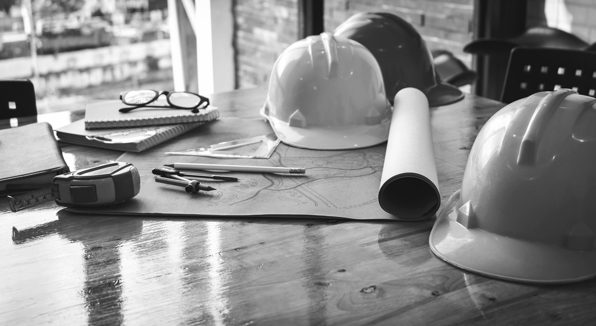Une photo en noir et blanc de casques de sécurité, d'un plan et d'autres outils de construction sur une table en bois.