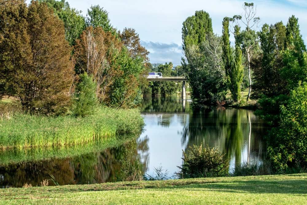 River Surrounded By Trees And Grass With A Bridge — Goulburn Solar In Queanbeyan, NSW