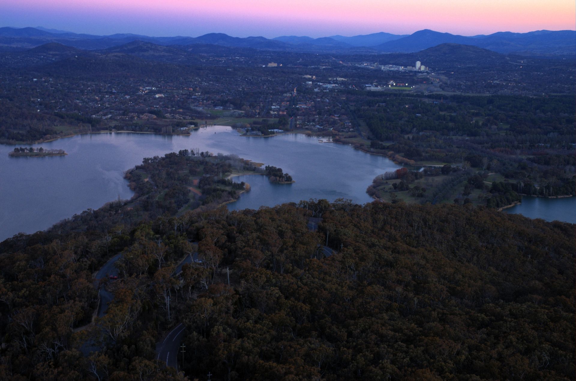 Lake and Forested Hills at Dusk With Pink Sky and Distant City Lights — Goulburn Solar In Woden Valley, ACT
