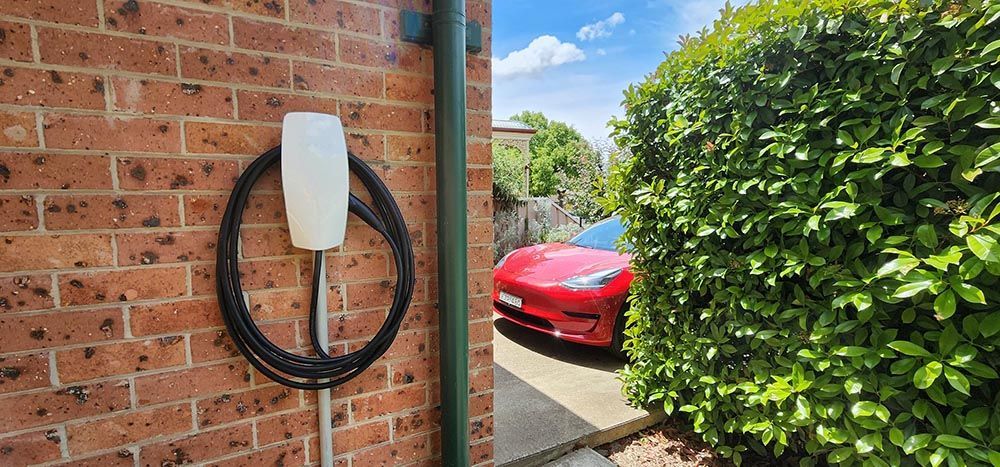 A Red Car Parked In Front Of A Brick Wall Next To A Hedge — Goulburn Solar In Goulburn, NSW