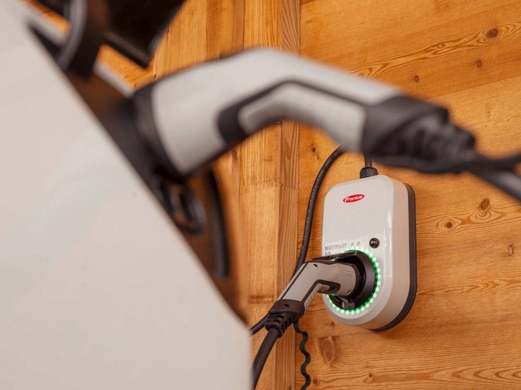 An Electric Car is Plugged Into a Charger on a Wooden Wall — Goulburn Solar In Goulburn, NSW