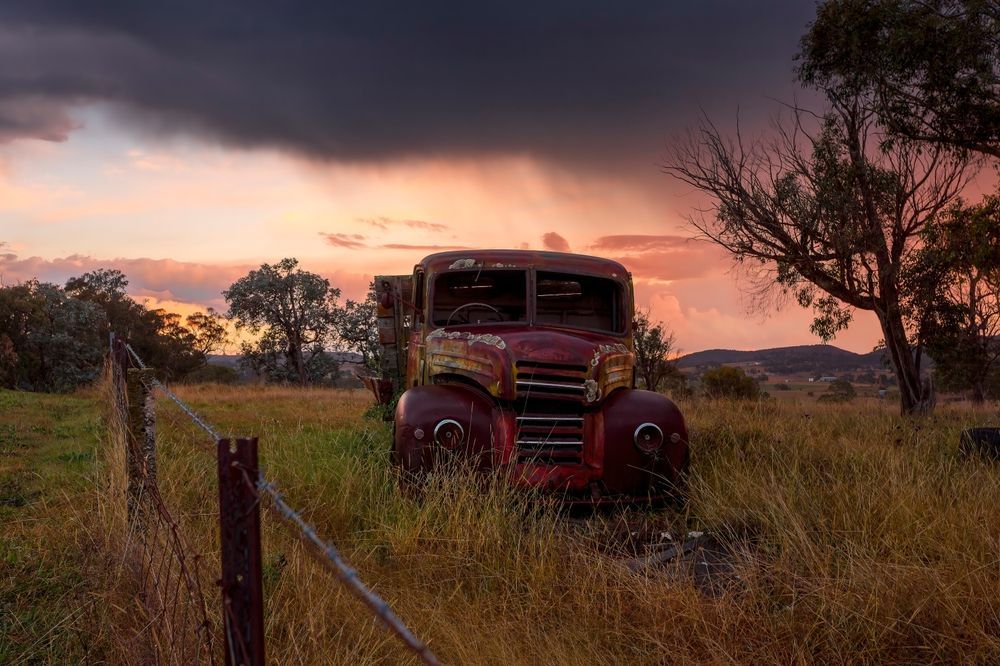 An Old Red Truck Parked In A Field At Sunset — Goulburn Solar In Marulan, NSW