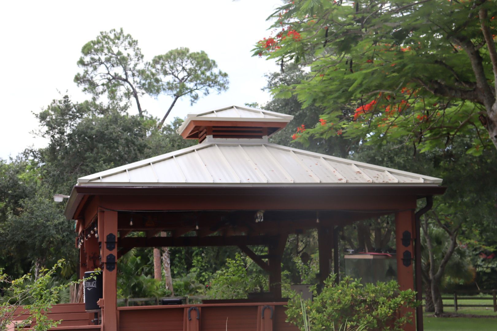 Wooden gazebo with a metal roof surrounded by lush green trees.
