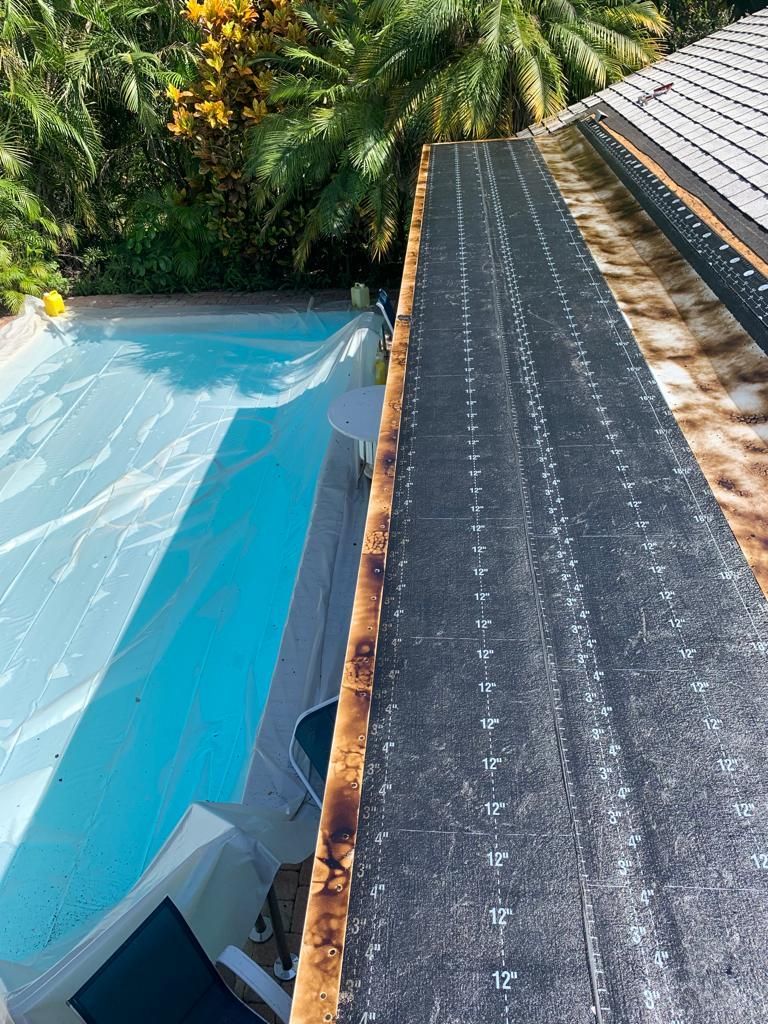 Poolside view of a roof with exposed black underlayment and a swimming pool.