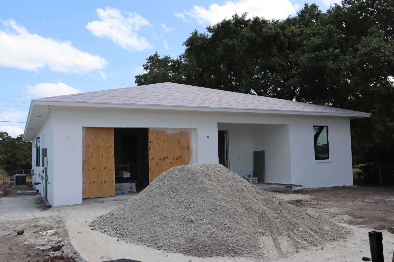 A white house under construction with a pile of gravel in front of the garage door.