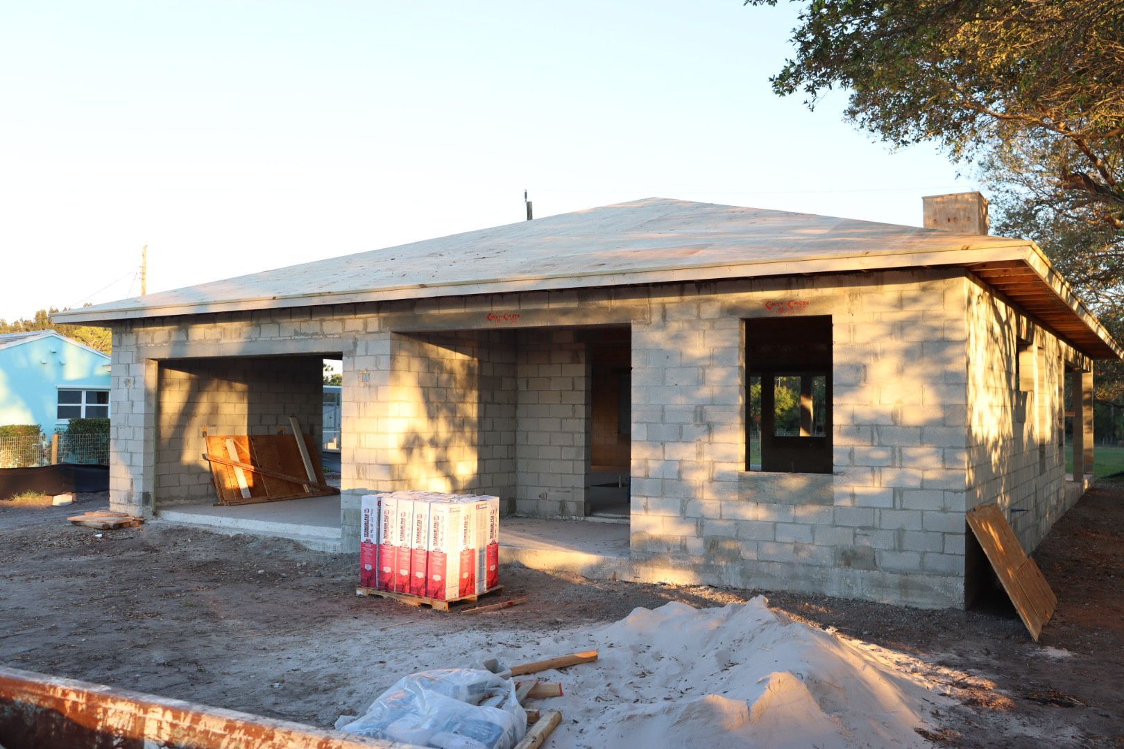 House under construction, concrete block walls, roof framing, and a pile of sand in the foreground.