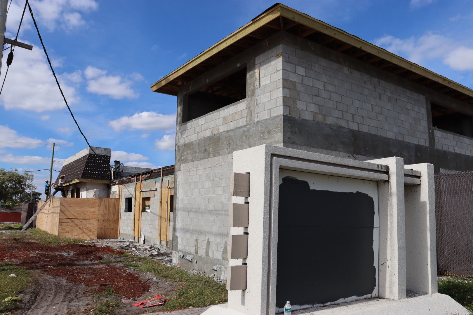 Construction site: two-story cinder block house with a partially built garage, blue sky in the background.