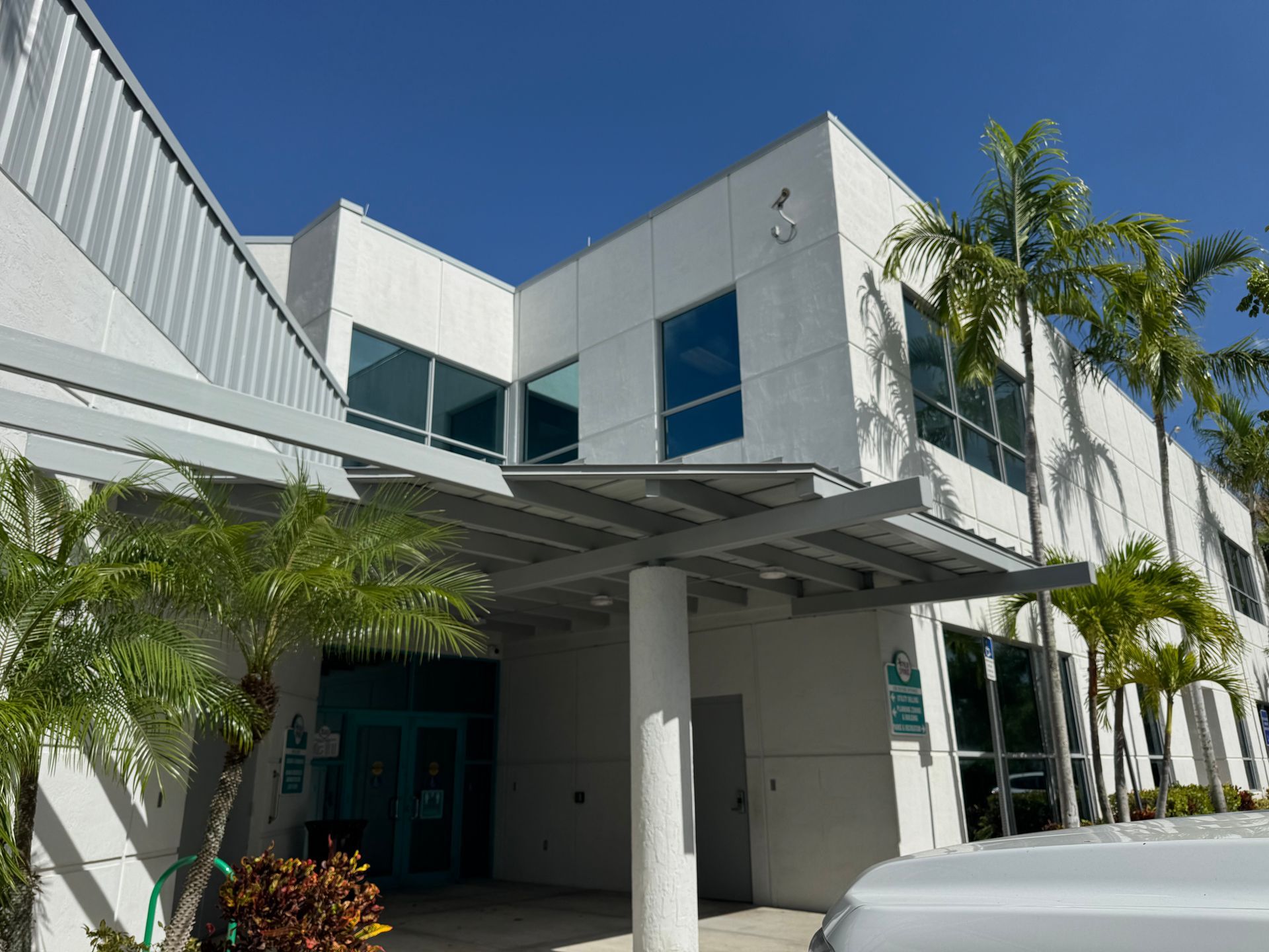 A white building entrance with awning, palm trees, and blue sky.
