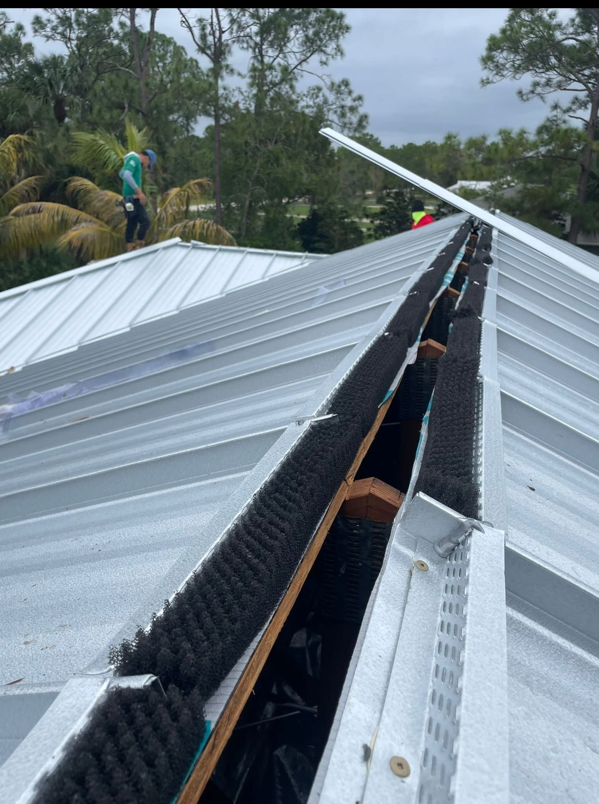 Metal roof with gutter guards; worker on roof repairs, trees in background.