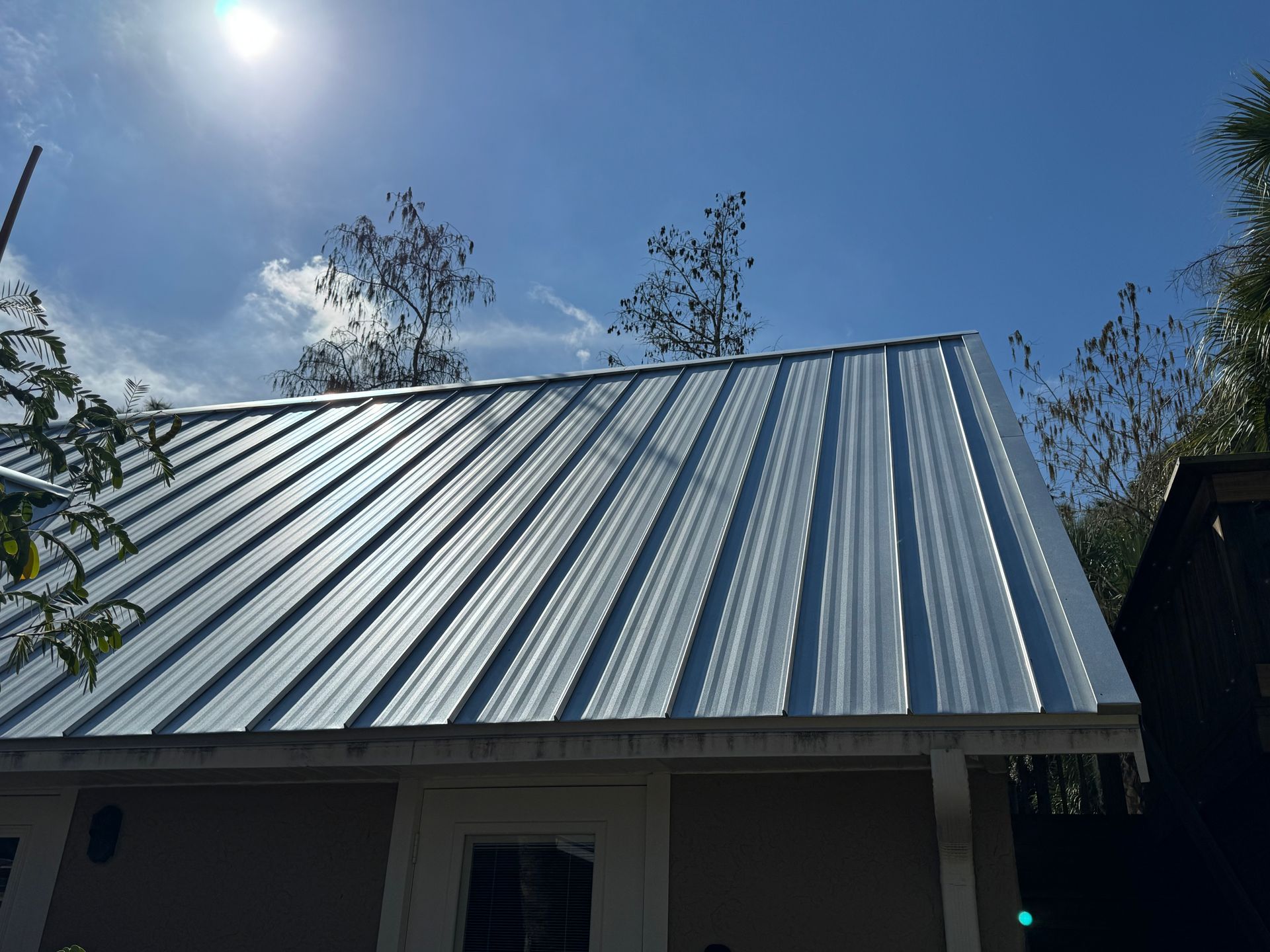 Shiny metal roof on a building under a blue sky. Sun is visible.